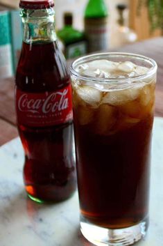 there is a drink on the table with ice and coke in front of it,