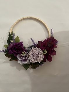 a wreath with purple flowers and greenery hanging from the side on a white wall