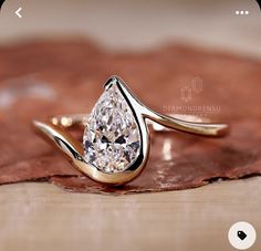 a pear shaped diamond ring sitting on top of a piece of wood next to a leaf