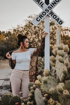 a woman leaning against a railroad crossing sign in front of cacti and succulents