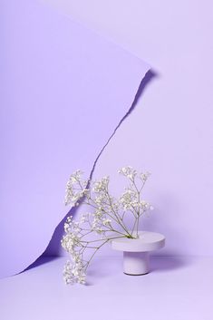 a white vase with flowers in it sitting on a table next to a purple wall