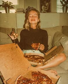 a woman sitting on a couch holding two pizzas