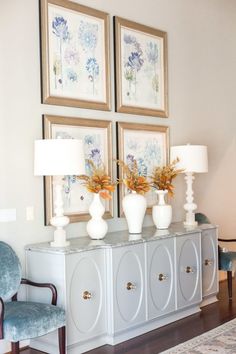 two white vases sitting on top of a dresser next to lamps and pictures above them