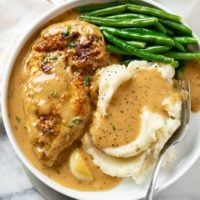 a white bowl filled with mashed potatoes and gravy next to green beans