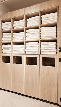 a room filled with lots of white sheets and folded ones on wooden shelves next to each other