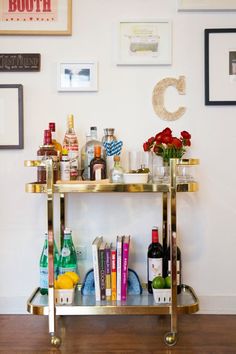 a gold bar cart filled with liquor bottles and glasses on top of a wooden floor