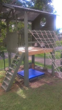 a wooden play structure with a blue mat under it and stairs leading up to the top