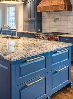 a large kitchen with blue cabinets and marble counter tops, an oven hood over the island