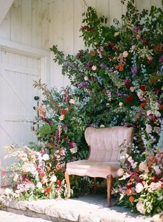 a pink chair sitting in front of a flower covered wall next to a wooden door