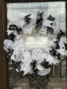 a wreath with black and white ribbons is displayed in front of a glass door that says sweet holiday