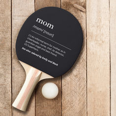 a ping pong paddle and ball on a wooden surface with the words mom printed on it