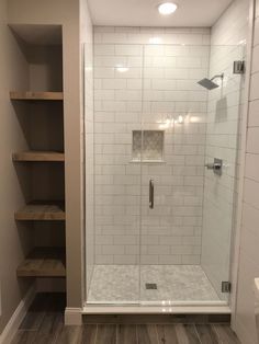 a walk in shower sitting inside of a bathroom next to a toilet and wooden shelves