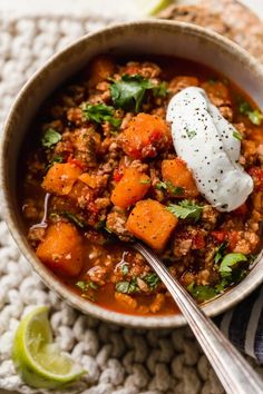 a bowl of chili and sweet potato soup with sour cream on top, next to a spoon