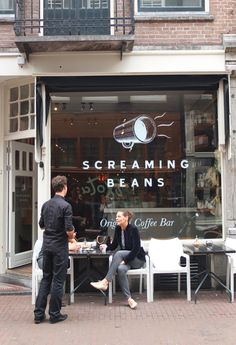 two people sitting at a table in front of a coffee shop with the words screaming beans on it