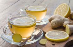 two cups of tea on a wooden table with ginger slices and other ingredients around them