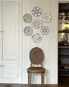 a chair sitting in front of a white wall with plates hanging on it's side