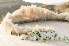 an arrangement of flowers and feathers on a wooden floor in front of a mountain range