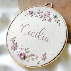 the embroidered name cecila is surrounded by pink flowers and hearts on a white satin background