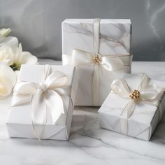 three white gift boxes with bows on them and flowers in the backgrouf