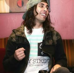 a young man sitting on top of a red couch wearing a hat and looking at the camera