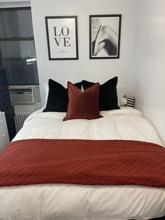 a bed with two framed pictures on the wall above it, and a red blanket