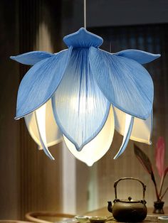 a blue flower hanging from a ceiling light in a living room with a kettle on the table