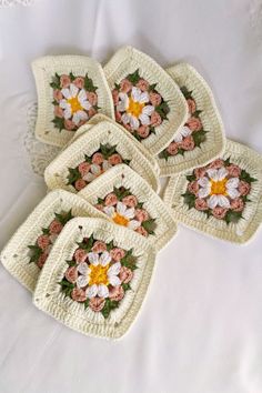 six crocheted coasters with flowers on them sitting on a white tablecloth