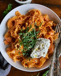 a white bowl filled with pasta and sauce on top of a wooden table next to silverware