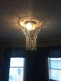 a basketball hoop hanging from the ceiling in front of two windows with curtains on them