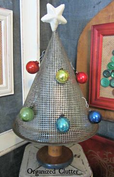 a metal christmas tree on top of a wooden stand in front of a framed picture