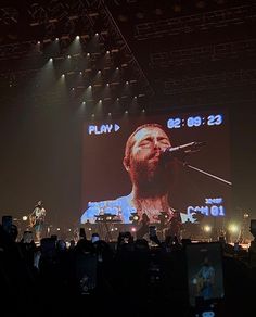 a large screen with a concert on it's side in front of a crowd