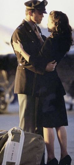 a man in uniform hugging a woman on the street next to a bag and suitcase