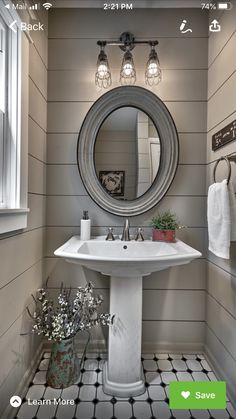 a white pedestal sink sitting under a round mirror in a bathroom next to a window