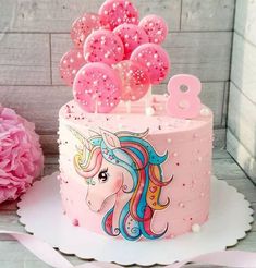 a pink birthday cake decorated with unicorns and balloons