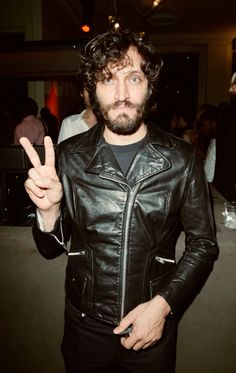 a man in a black leather jacket is making the peace sign with his hand while standing next to other people