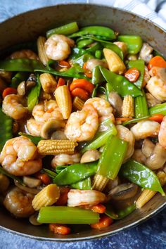 stir fry with shrimp, corn and vegetables in a skillet on a blue surface