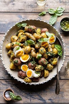 a bowl filled with potatoes and boiled eggs on top of a wooden table next to two glasses