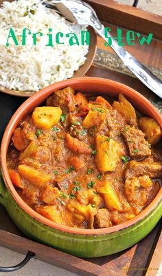 an african beef stew in a bowl with rice and spoons on the side next to it