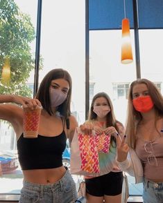 three young women wearing face masks and holding shopping bags in front of a large window