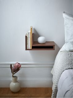 a shelf with books on it next to a flower vase and other items in front of a bed