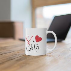 a white coffee mug sitting on top of a wooden table next to a laptop computer