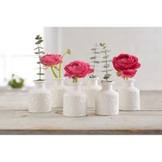 five white vases with pink flowers in them on a table top, one is empty