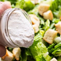 a person dipping dressing into a salad with lettuce and croutons on top