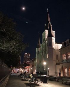 an old church lit up at night with people sitting on benches in the foreground