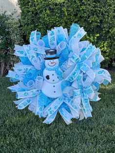 a snowman wreath on the grass in front of some bushes and bushes with blue ribbons