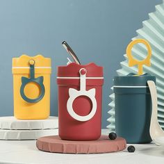 three different colored containers on a table with spoons and utensils in them