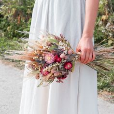 a woman in a white dress holding a bouquet of dried flowers and grass with her hands