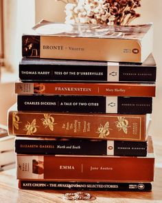 a stack of books sitting on top of a wooden table next to a vase with flowers