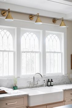 a kitchen with two sinks and three windows in the wall above them is also white marble countertops