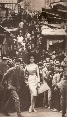 an old black and white photo of a woman in a large hat surrounded by people